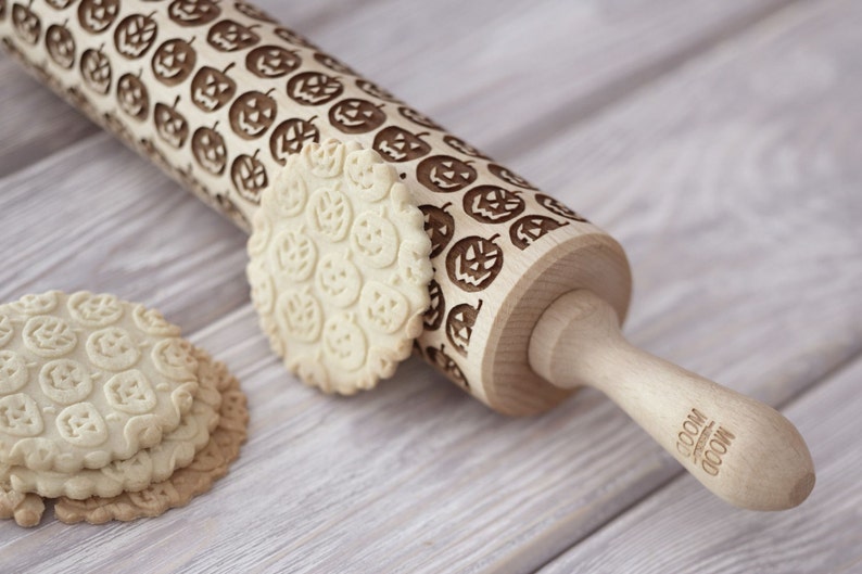 A pile of well baked cookies with embossed design is in front of a rolling pin