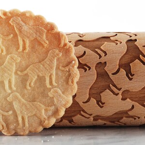 May include: A wooden rolling pin with a dog silhouette design. The rolling pin is used to create dog-shaped impressions in dough. A cookie with dog-shaped impressions is shown next to the rolling pin.