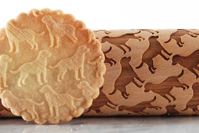 May include: A wooden rolling pin with a dog silhouette design. The rolling pin is used to create dog-shaped impressions in dough. A cookie with dog-shaped impressions is shown next to the rolling pin.