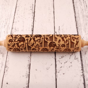 Wooden rolling pin laser engraved with design of tropical animals such as elephants, giraffs, parrots, monkeys, surrounded by palm and monstera leaves.