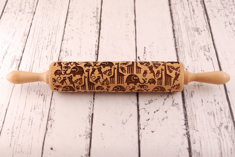 Wooden rolling pin laser engraved with design of tropical animals such as elephants, giraffs, parrots, monkeys, surrounded by palm and monstera leaves.