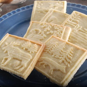 Cookies made with the rolling pin. rectangular,each has a different animal on it. Cookies are lying on the dark blue plate, standing on a silverplated metal dish with decorative art nuveau rim.