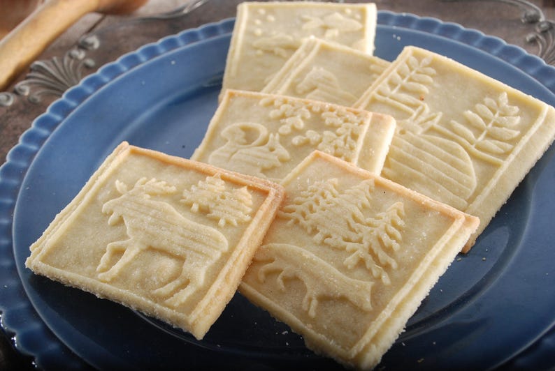 Cookies made with the rolling pin. rectangular,each has a different animal on it. Cookies are lying on the dark blue plate, standing on a silverplated metal dish with decorative art nuveau rim.