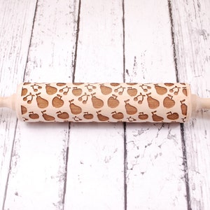 Wooden rolling pin with embossing design of apples, pears and cherries. The backgroundare white rustic boards.