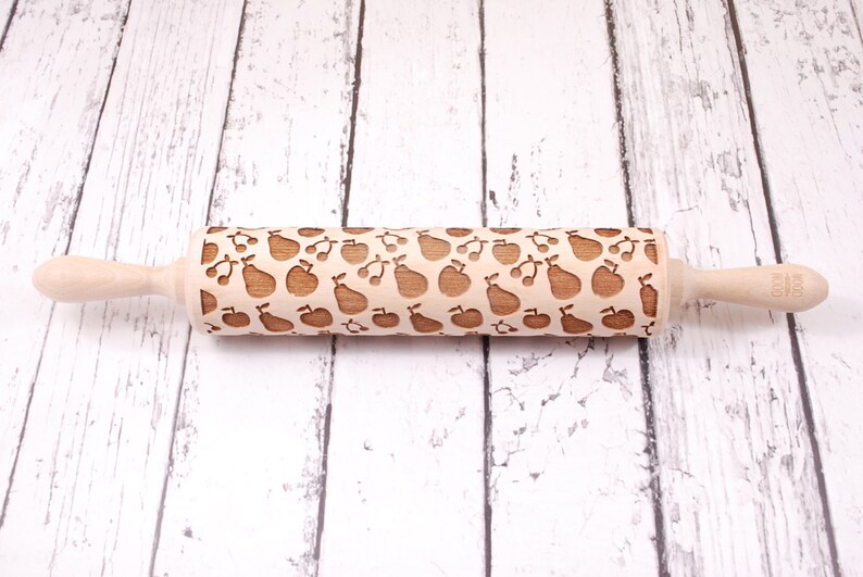 Wooden rolling pin with embossing design of apples, pears and cherries. The backgroundare white rustic boards.