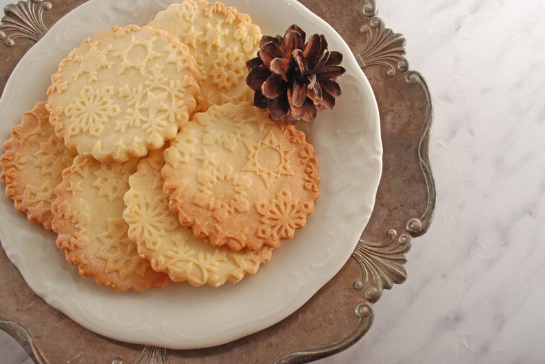 Seeral round biscuits with embossed snowflakes design aro one the white porcelain plate, that is lying on silerplated metal dish.