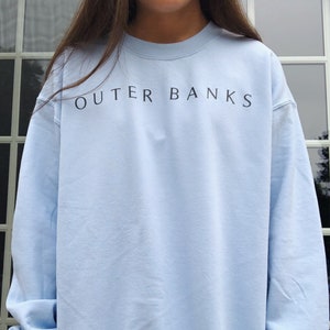 May include: A light blue sweatshirt with the text "OUTER BANKS" printed in black on the front.