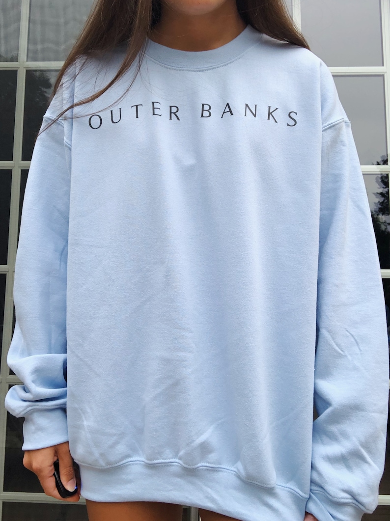 May include: A light blue sweatshirt with the text "OUTER BANKS" printed in black on the front.
