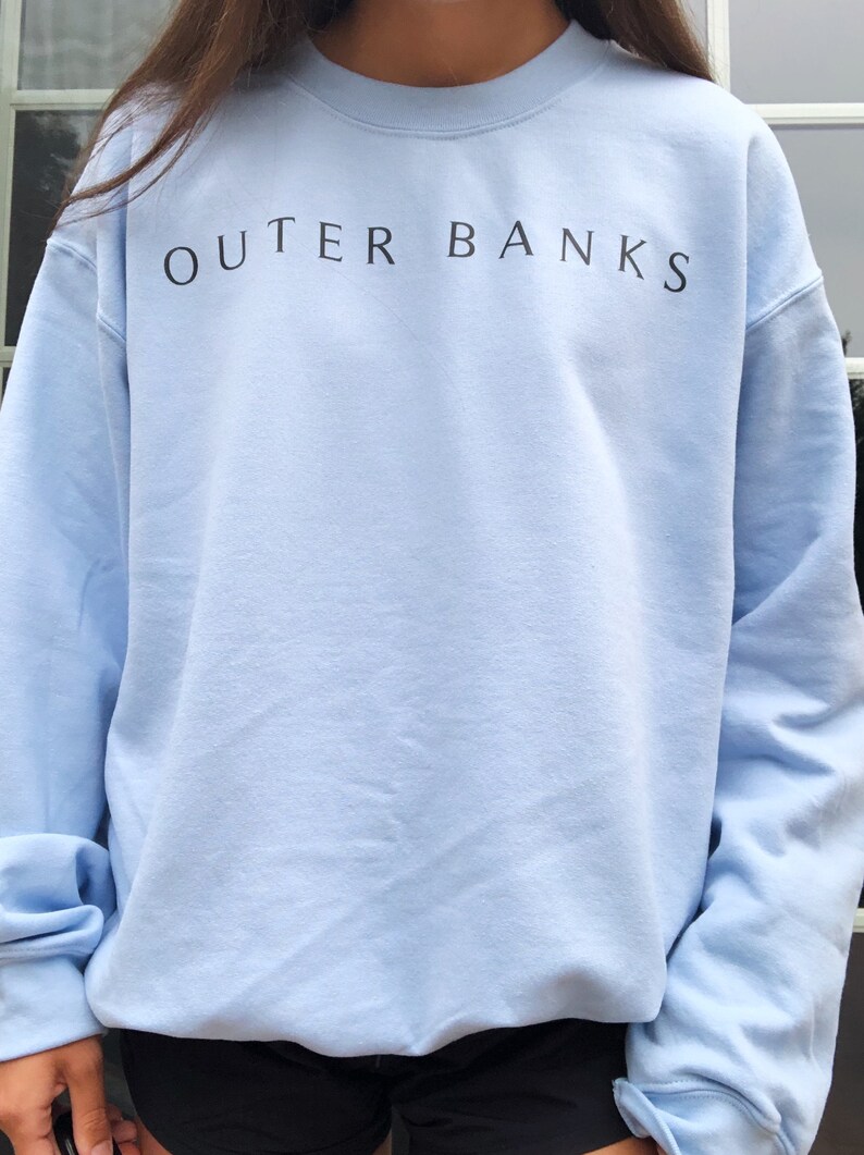 May include: A light blue sweatshirt with the text "OUTER BANKS" printed in black on the front.