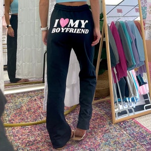 May include: Black sweatpants with a white graphic that says "I love my boyfriend" with a pink heart.