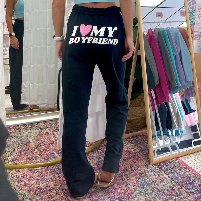 May include: Black sweatpants with a white graphic that says "I love my boyfriend" with a pink heart.