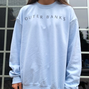 May include: A light blue sweatshirt with the text "OUTER BANKS" printed in black on the front.