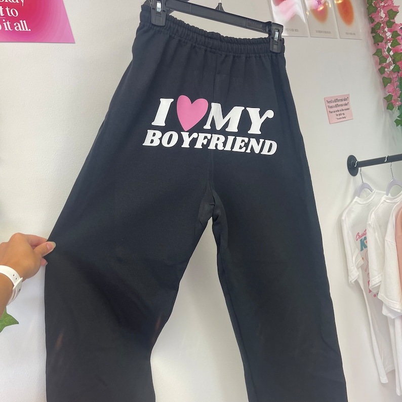 May include: Black sweatpants with a white graphic that says "I love my boyfriend" with a pink heart.