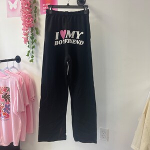 May include: Black sweatpants with a white graphic that says "I love my boyfriend" with a pink heart.