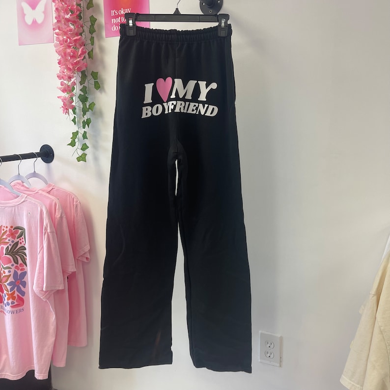 May include: Black sweatpants with a white graphic that says "I love my boyfriend" with a pink heart.