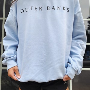May include: A light blue sweatshirt with the text "OUTER BANKS" printed in black on the front.
