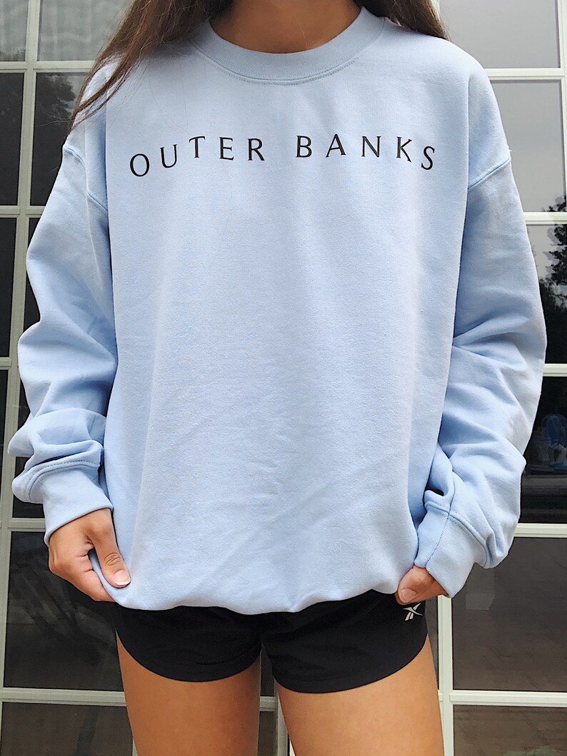 May include: A light blue sweatshirt with the text "OUTER BANKS" printed in black on the front.