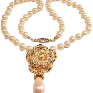 May include: A vintage pearl necklace with a gold-tone floral pendant and a teardrop-shaped pearl drop. The necklace features a strand of cream-colored pearls and a gold clasp. The pendant is intricately detailed with a flower design.