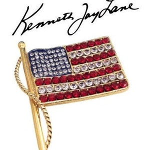 May include: A gold-toned brooch in the shape of an American flag. The flag is made of red, white, and blue rhinestones. The brooch is signed "Kenneth Jay Lane".
