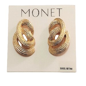 May include: A pair of gold-tone Monet earrings with a twisted knot design. The earrings are displayed on a white card with the word "MONET" printed in black.