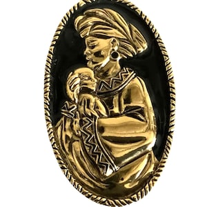 May include: Gold-toned oval brooch with a black enamel background. The brooch depicts a woman holding a child, both with detailed features and intricate designs.
