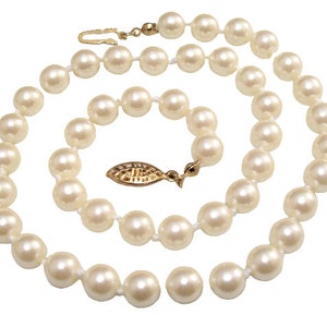 May include: A strand of white pearl necklace with a gold clasp and a small gold leaf charm.