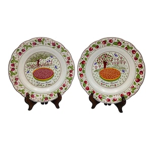 May include: Two white ceramic plates with scalloped edges, each featuring a central illustration of a fruit tart and a tree. One plate displays a strawberry tart with the text Tarte aux Fraises, while the other shows an apple tart with Tarte aux Pommes.