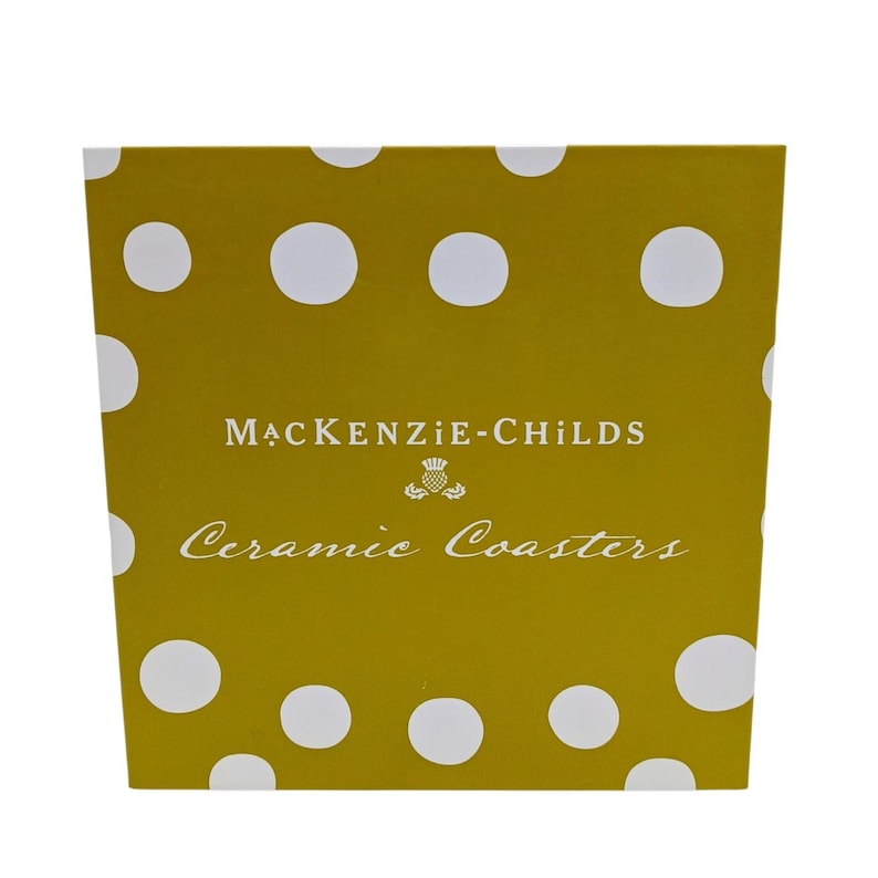 May include: A square mustard yellow box with white polka dots. The text MACKENZIE-CHILDS is printed in white, followed by a small thistle icon and the words Ceramic Coasters in a white script font centred on the front of the packaging.