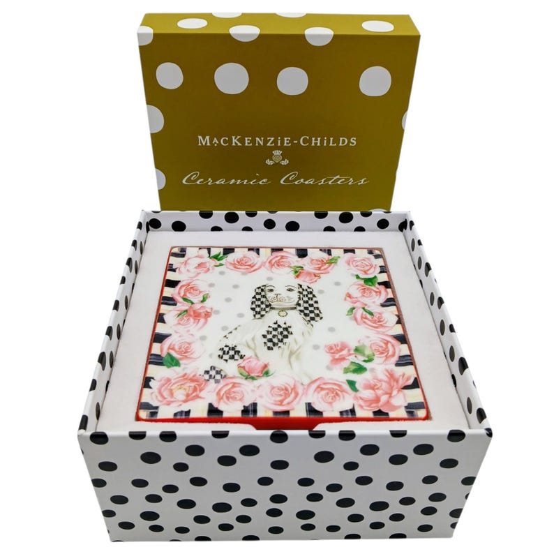 May include: A square ceramic coaster featuring a central illustration of a spaniel dog with black and white chequered ears, surrounded by pink roses and a black and white striped border, housed in a white box with black polka dots.