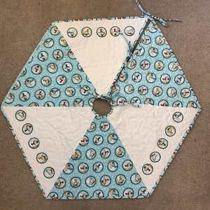 May include: A hexagonal white and blue quilted Christmas tree skirt with a snowman pattern. The skirt has a white center with a hole for the tree trunk.