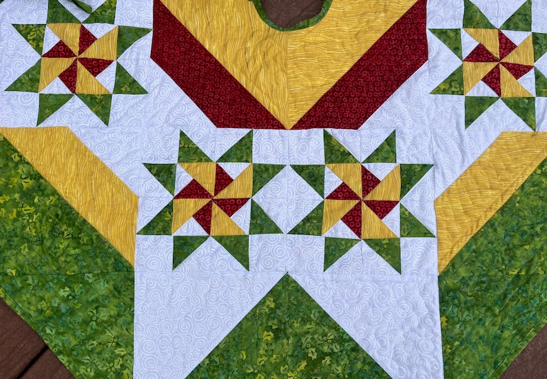 May include: A Christmas tree skirt with a white background and a pattern of green, red, and yellow stars. The skirt has a scalloped edge.