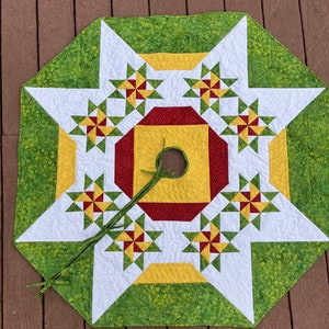 May include: A green, white, red, and yellow quilted Christmas tree skirt with a star design and a hole in the center for a tree stand.