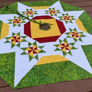 May include: A green, white, red, and gold quilted Christmas tree skirt with a starburst design. The skirt has a center hole for the tree trunk.