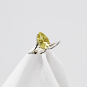 Puede incluir: Un anillo de plata con una piedra preciosa amarilla en forma de pera engastada en una banda delicada y retorcida.