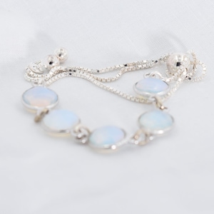Puede incluir: Un brazalete de cadena de plata con cinco piedras de ópalo blanco. El brazalete tiene un cierre deslizante para un tamaño ajustable.