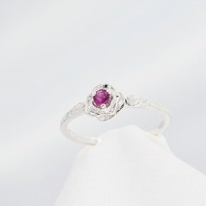 May include: A silver ring with a pink gemstone set in a rose-shaped design. The ring has delicate leaf accents on either side of the rose.