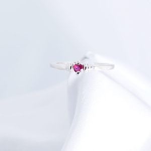 May include: A silver ring with a small, round, pink gemstone set in the center.