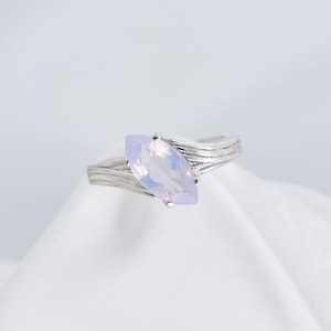 May include: A silver ring with a light purple marquise-shaped gemstone. The ring band has a wavy design.