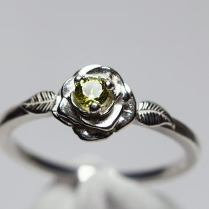 May include: A silver ring with a delicate rose design and a small green gemstone in the center.