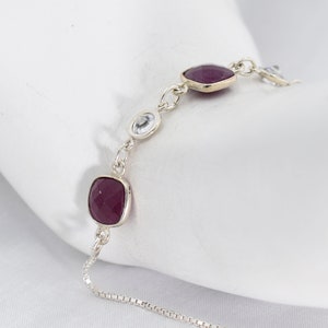 May include: A silver chain bracelet with two square-shaped purple gemstones and two round clear gemstones.