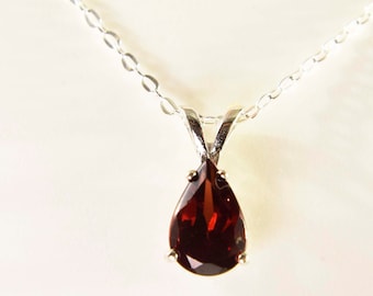 May include: A silver chain necklace with a pear-shaped red gemstone pendant.