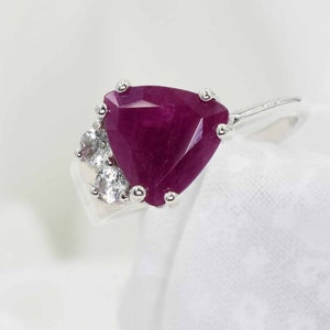May include: A silver ring with a large, triangular ruby gemstone and smaller, round white gemstones.