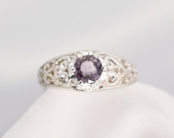 May include: A silver ring with a delicate filigree design and a round, purple gemstone in the center.