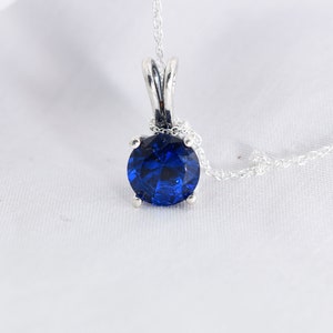 May include: A silver necklace with a blue gemstone pendant. The pendant is round and has a faceted design.