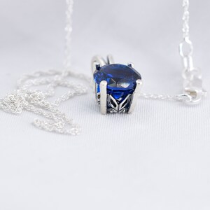 May include: A silver chain necklace with a blue gemstone pendant. The pendant is set in a silver filigree design.