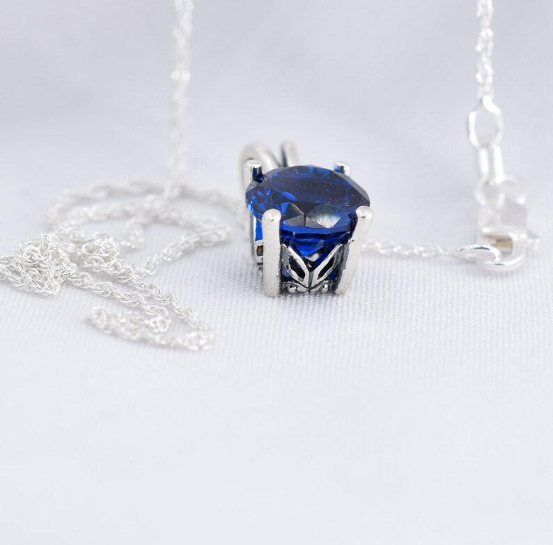 May include: A silver chain necklace with a blue gemstone pendant. The pendant is set in a silver filigree design.
