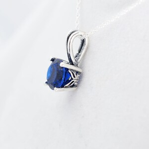 May include: A silver pendant necklace with a blue gemstone set in a silver prong setting.