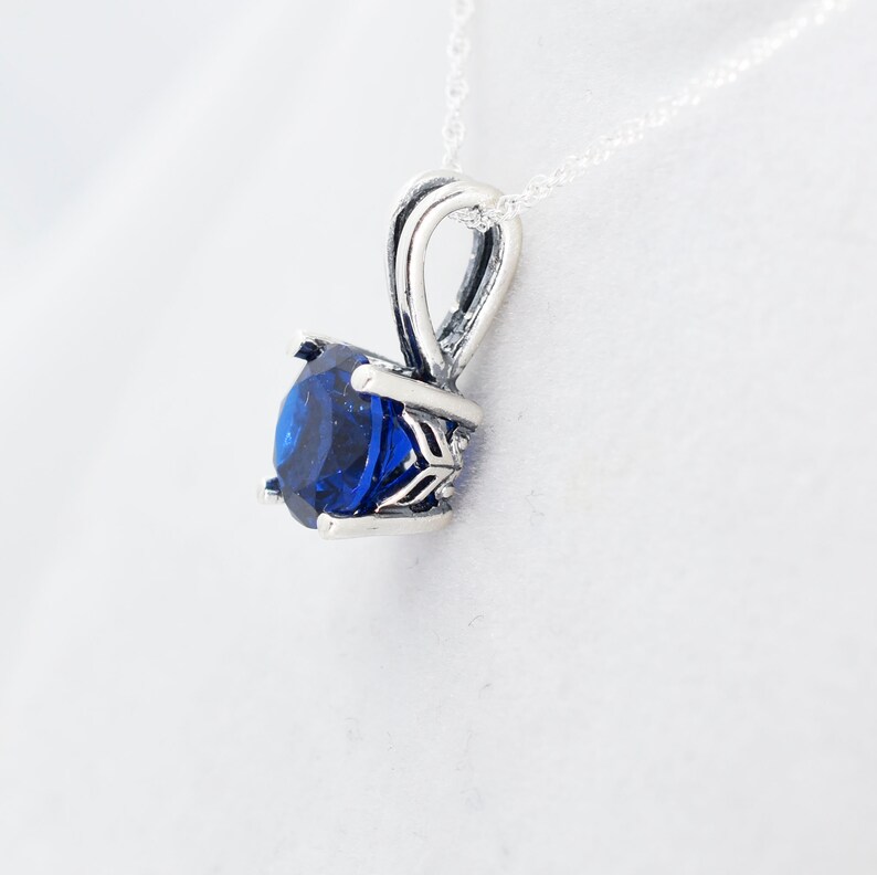 May include: A silver pendant necklace with a blue gemstone set in a silver prong setting.