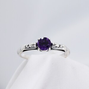 May include: A silver ring with a purple amethyst gemstone set in a delicate, ornate design.
