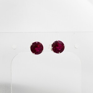 May include: A pair of silver stud earrings with round, deep red gemstones.